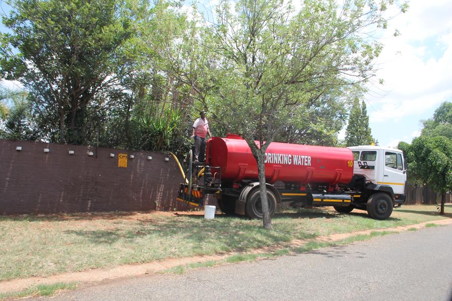 The truck and its driver busy pumping water through a hose over the wall of the private house.