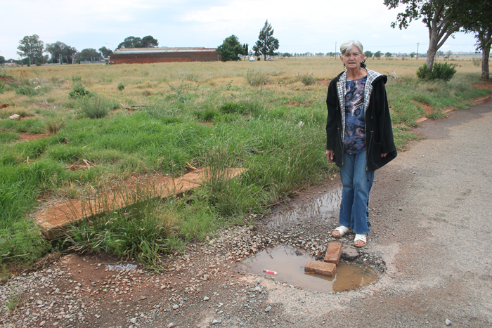 Ms Louise Combrink next to the sidewalk where the long grass suggests that the leak has been there for a long time.