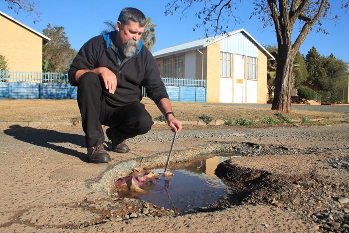 Mr Jeff Ralph shows how deep one of the potholes is. This hazard will seriously damage a car's wheel if the driver should hit it.