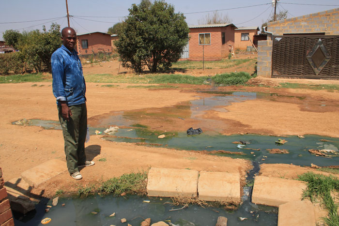 Mr David Ndubatha stands between pools of sewage is leaking from manholes on either side of the road in front of his house.