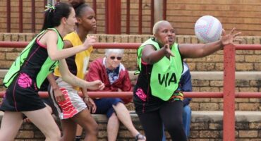 'n Toeskouer kyk aandagtig hoe spelers van die Warriors en Hoërskool Carletonville vir beheer van die bal veg.