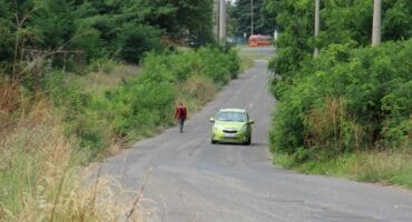 Pedestrians are forced to walk on the road in front of approaching vehicles due to the sidewalks being overgrown.