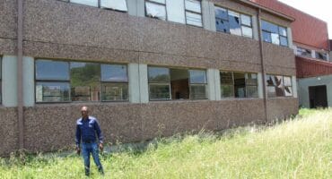 Concerned community member Ayanda Tobo and the damaged back of the school.