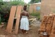 Nandipha Rudaza looks into her neighbouring yard, where criminals are regularly hiding in the house damaged by the sinkhole. She is standing next to the door of her family's house that was smashed by the criminals when they broke in.