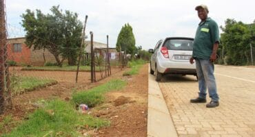 Kabelo Klaas Masebeni shows how the sidewalk and street is much higher than his yard.