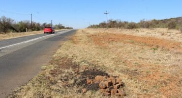 A motorist drives past several heaps of partially buried tar on the side of the road. Photo: Adele Louw (Carletonville and Fochville Herald)