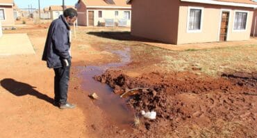 Mzwandile Kheswa of the Elderly Movement For Change pointed out various problems, such as a water leak at house no. 9163 in Ext 6. Photo: Adele Louw (Carletonville and Fochville Herald)