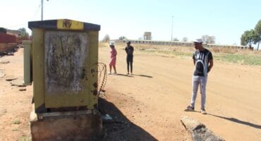 Concerned residents looking at a damaged electricity box with the Khutsong hostels in the background. Photo: Adele Louw (Carletonville and Fochville Herald)