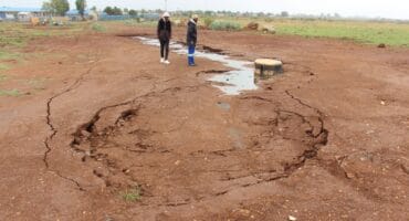 A large amount of sewage was leaking from the collapsing manhole and adjacent pipeline. Hlanganani Primary School is in the background. Insert: By October 5, the municipality or its contractor had dug a channel to reroute the leaking sewage. Photo: Adele Louw (Carletonville and Fochville Herald)