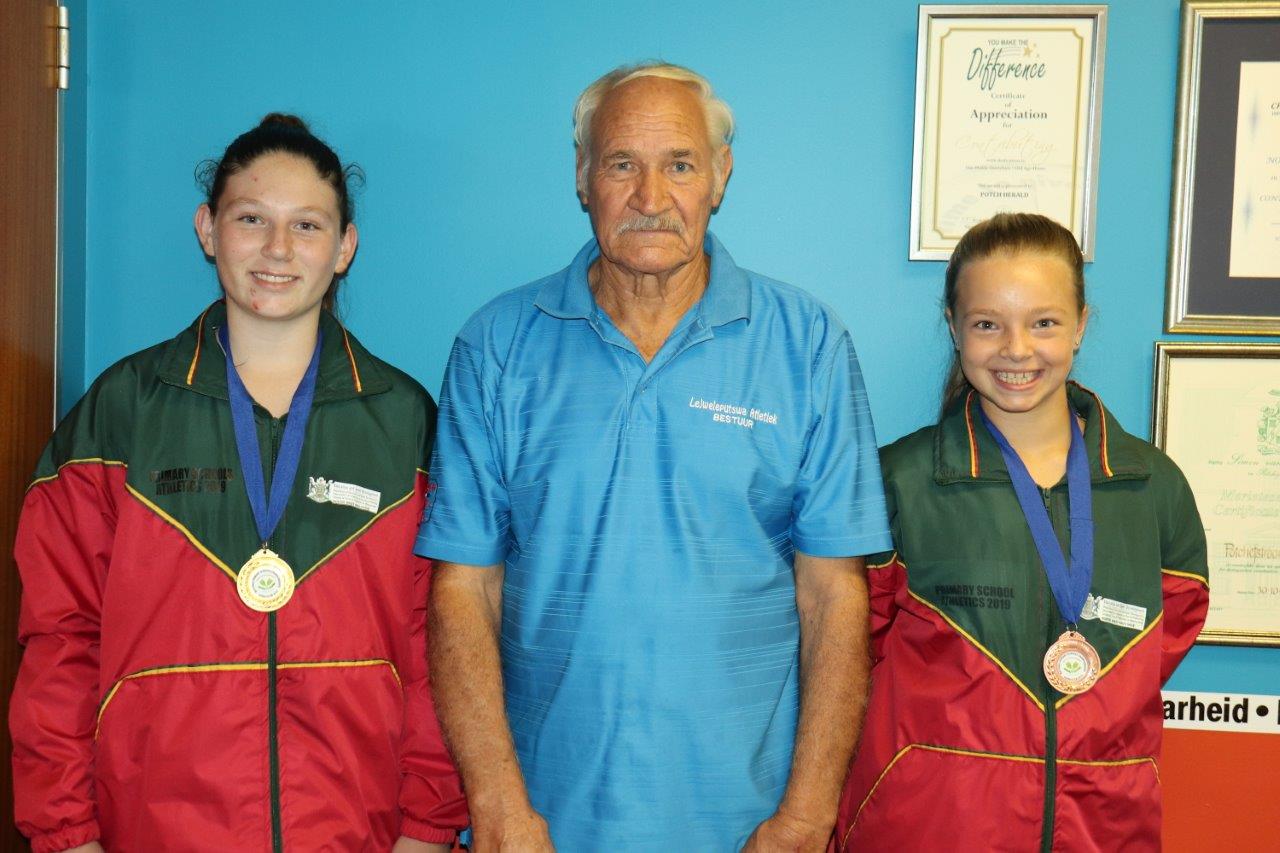 Die bekende Potchefstroomse atletiekafrigter, Theuns Naudé, saam met atlete wat medaljes by die Suid-Afrikaanse Skole Atletiekkampioenskappe ingepalm het. Links is Jamoré Olivier en regs Martiné van Aswegen.