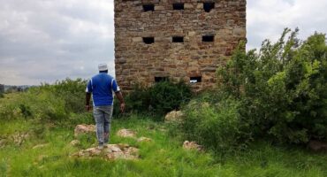 Ancient stone structure in Sedibeng area surrounded by green grass and bushes, with a man observing the site.