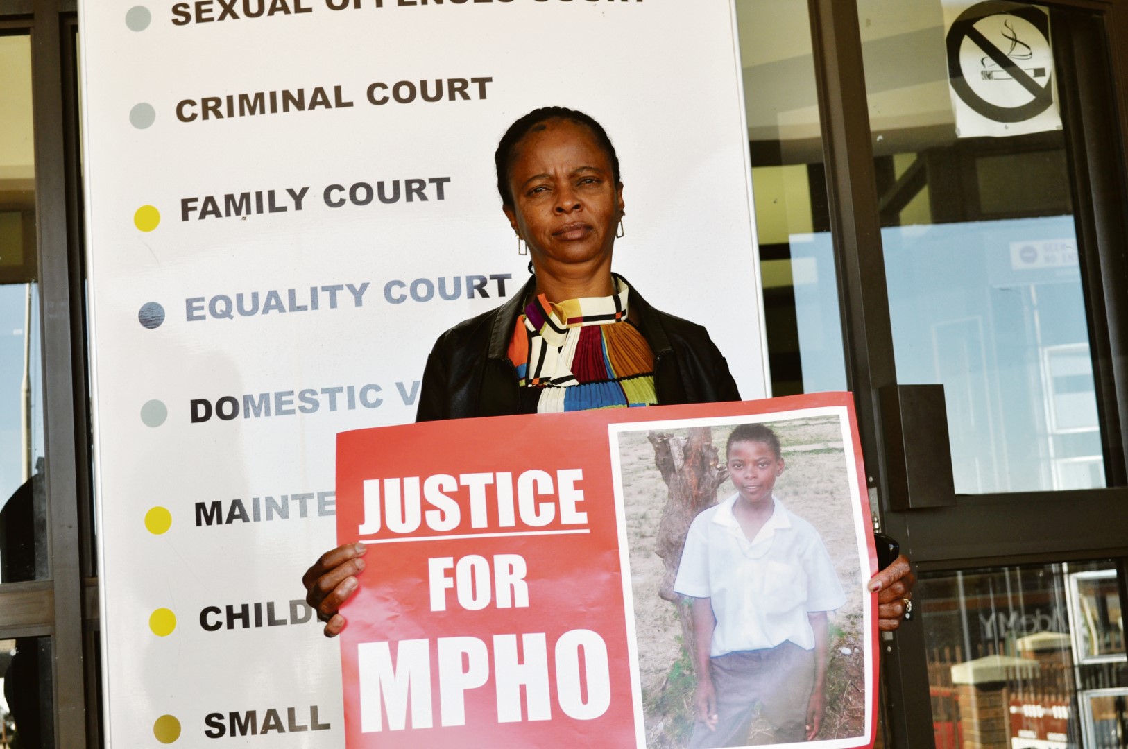 Ms Kapu Abrahams, the mother of Mpho “Gift” Abrahams, the murdered teen, holding up a placard during the court appearance of the suspects. Photo: Victor Boqo.