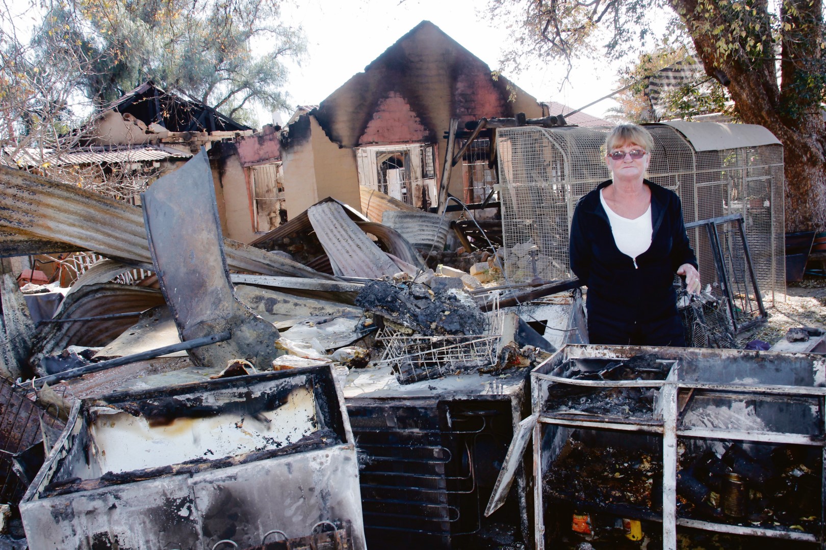 Susan de Wet by die verbrande inhoud van hul huis nadat hulle alles verloor het behalwe die slaapklere wat sy die aand van die brand aangehad het. Die egpaar het selfs hul geliefde diere-kinders in die brand verloor. Foto: Teresa Holloway