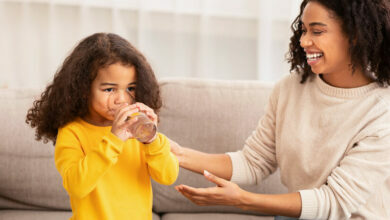 Woman Giving Daughter Glass Of Water Sitting On Sofa Indoor
