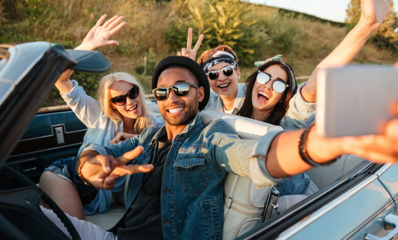 Happy young people taking selfie with smartphone in the car