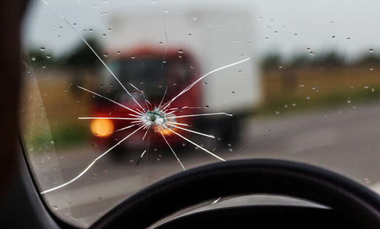 Broken windshield of a car. A web of radial splits, cracks on the triplex windshield. Broken car windshield, damaged glass with traces of oncoming stone on road or from bullet trace in car glass
