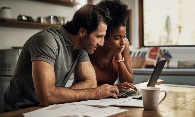 Couple with a laptop doing finance paper work, paying debt insurance loans or online ebanking together at home. Two serious people planning and looking at financial document, bills rate for mortgage