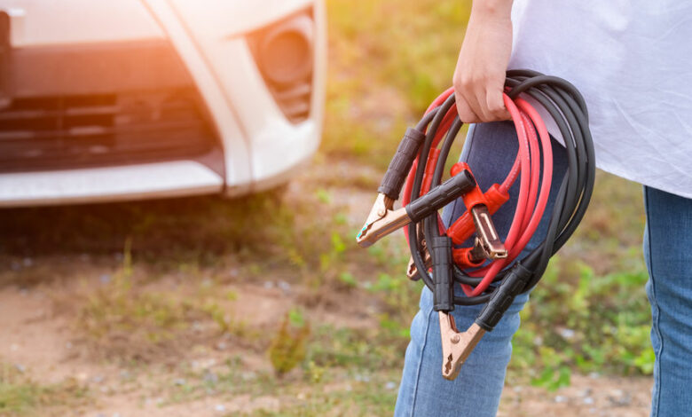 Closeup of woman hand holding battery cable copper wire for repairing broken car by connect battery with red and black line to electric terminal by herself. Car maintenance and transportation concept