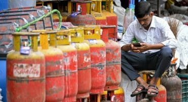 A man uses a mobile phone next to liquefied petroleum gas (LPG) cylinders outside a shop in Bengaluru on June 2, 2026 amid global energy crisis triggered by the Middle East war. (Photo by Idrees MOHAMMED / AFP)