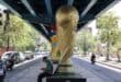 An Iranian man sits beneath a World Cup trophy displayed under a bridge in Tehran on June 7, 2026.