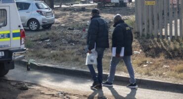 Graphic content / Crime scene investigators walk near a body of a victim laying in the road at Jumpers informal settlement in Cleveland, east of Johannesburg, on June 10, 2026.