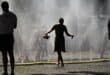 People stand near over water hoses spilling water to provide relief from the summer heat as part of Cologne’s climate adaptation measures in Cologne, western Germany on June 25, 2026 during a heatwave in Europe.