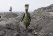 Sandra Tavares balances a bucket full of water on her head past piles of black sand at a beach depleted by sand mining for commercial sale near Ribeira da Barca, on May 20, 2026. Photo: AFP