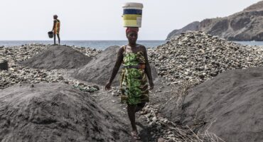 Sandra Tavares balances a bucket full of water on her head past piles of black sand at a beach depleted by sand mining for commercial sale near Ribeira da Barca, on May 20, 2026. Photo: AFP