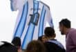 Argentina fans gather beneath a giant Argentina jersey bearing Lionel Messi's number 10 displayed in front of the National Flag Memorial in Rosario, Santa Fe province, Argentina, on July 18, 2026, ahead of the 2026 FIFA World Cup final between Argentina and Spain on July 19. (Photo by Marcelo Manera / AFP)