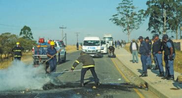 Firefighters extinguish burning tyres and clear rubble from Lion Park Road after residents blocked the route in protest yesterday. Photo: Moeketsi Mamane