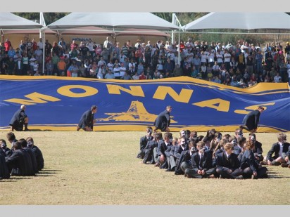 Monnas-leerlinge dra 'n banier met die skoolwapen op die veld.