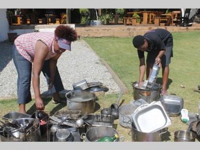 Sheila Mupfuri en Rachek Ndlovu, kelners van Jenny's Pub, besig om van die swart gebrande kombuisware te was.