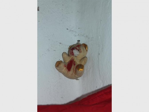 A teddy bear stained with red paint pinned against the wall.