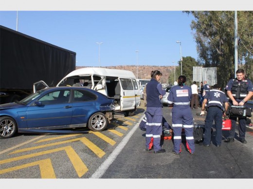 Ambulance personnel tend to the drivers of the damaged vehicles while the minibus taxi and a blue BMW block the road.