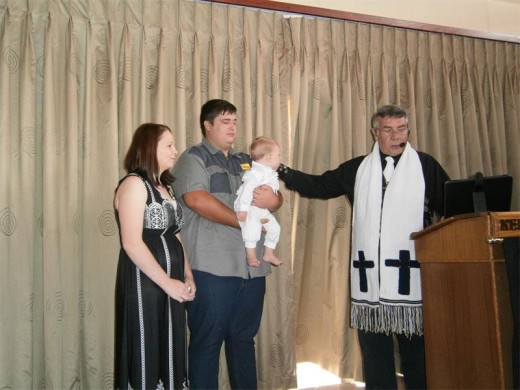 Pastoor Fanie doop klein Juan met ouers Rochelle en Rynhardt wat hom vashou.