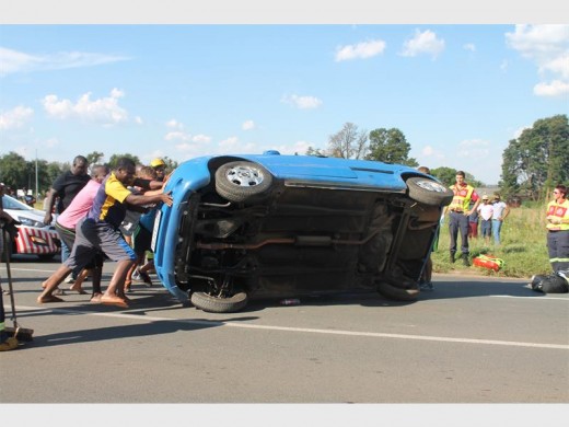 Members of the community help turn the overturned vehicle back on the road to be towed.