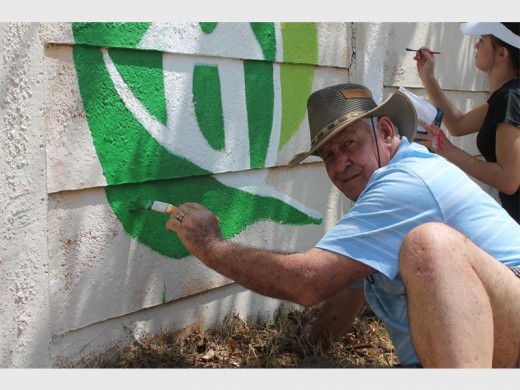 Jakkie Naudé gee 'n helpende hande en verf die Mug and Tree se embleem op die parkie se muur.
