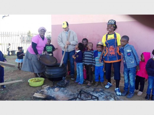 Volunteers Thokoza and Ennie, with Shabier Dabhelia (centre)  flanked by a number of children while cooking. Photo: Submitted.