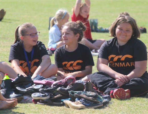 Somari Ryan, Samantha Henriques en Chaniqé Marais sit op Kennies se rugbyveld voor 'n hoop skoene wat in die vorm van 'n voet gepak is.