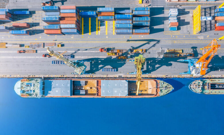 Aerial top view huge cargo ship moored at the pier at the port, loading goods, metal, concrete and other solid raw materials.