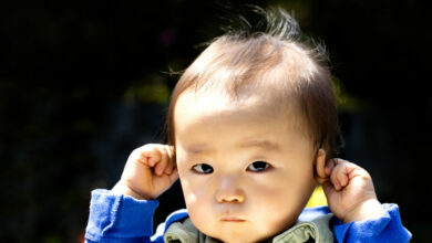Baby touching his ears isolated on a black background and outdoors. Or hear no evil