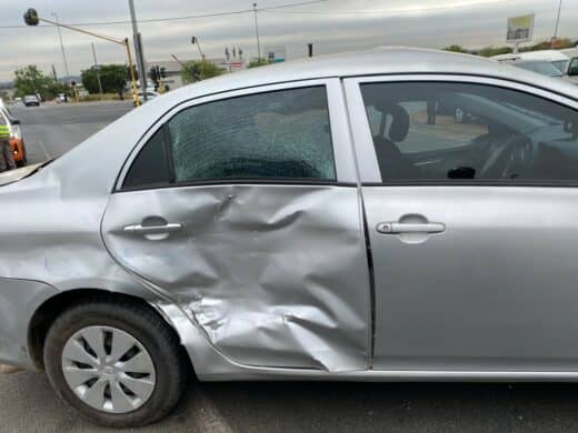 A silver car featuring a damaged door, indicating recent impact.
