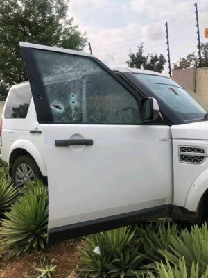 White SUV in a garden, riddled with bullet holes.