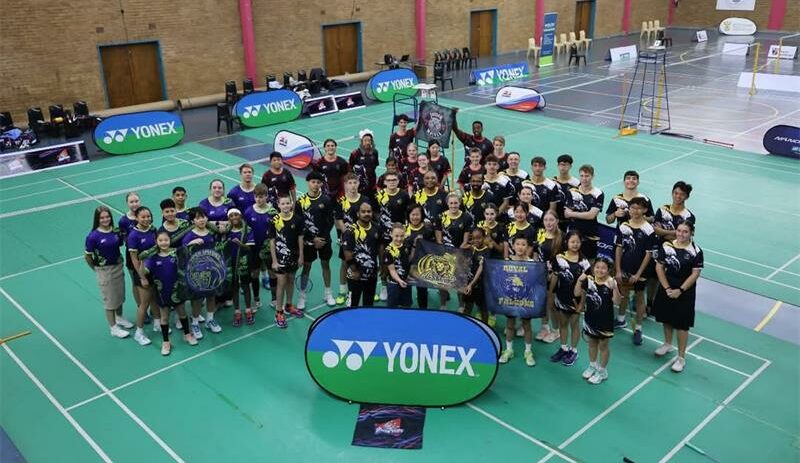 A group of people posing for a photo in a badminton court.