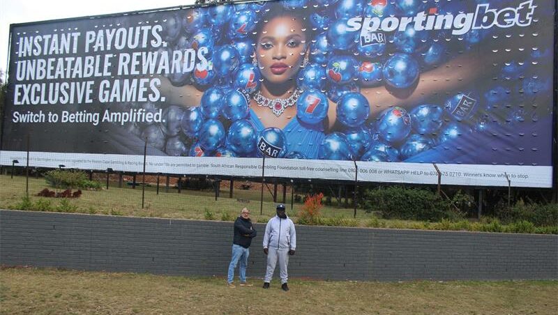 Maj Saffari and Rufas Mazwazi by the gambling billboard near the Cedar Road and Riverside Drive intersection opposite Steyn City School on June 4, 2026. Photo: Ayanda Ntshingila