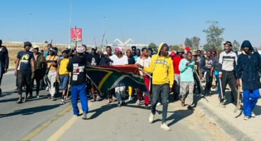 Young protesters march along Winnie Mandela Drive in Diepsloot, chanting ‘maba hambe’ meaning ‘they must go’ as they carry the South African flag. Photo: Ditiro Masuku