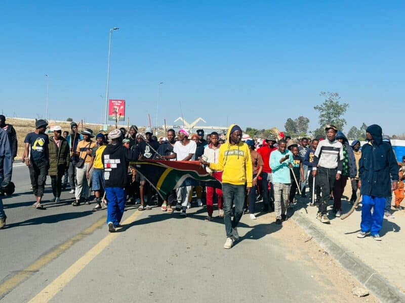 Protesters march along Winnie Mandela Drive in Diepsloot, as they hold the South African flag. Photo: Ditiro Masuku