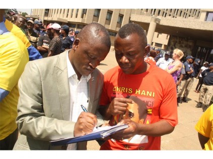 One of the community leaders Solly Nonyane and the crowd looked on as Vincent Hlatshwayo signs the memorandum of grievances. Hlatshwayo is from the office of the MMC for Corporate and Shared Services, Phelisa Nkunjana.