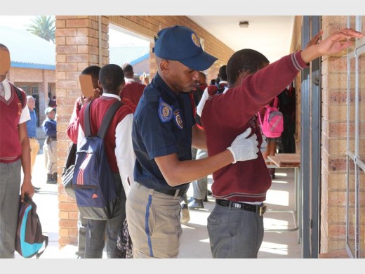 A metro police officer conducting a body search on a boy learner.