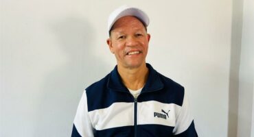 A man wearing a white cap and a Puma jersey stands in front of a plain white background.